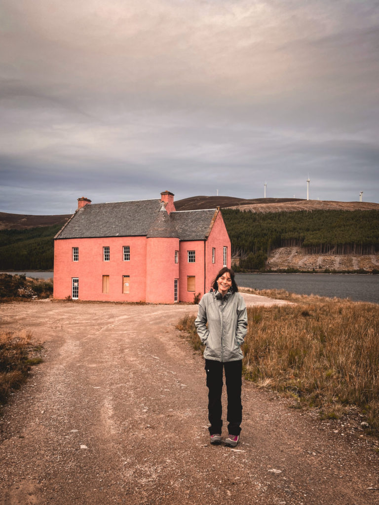 Girl standing in front of pink house by Loch Glass